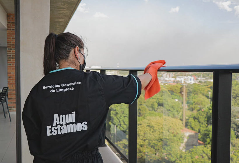 Profesional de Aquí Estamos con uniforme de la marca limpiando la baranda de un balcón con vista a Asunción